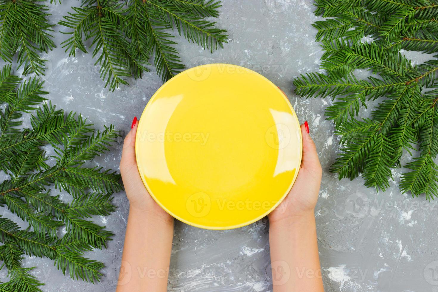 female hands holding an empty yellow plate on a gray background with Christmas branches. view from above for your design photo