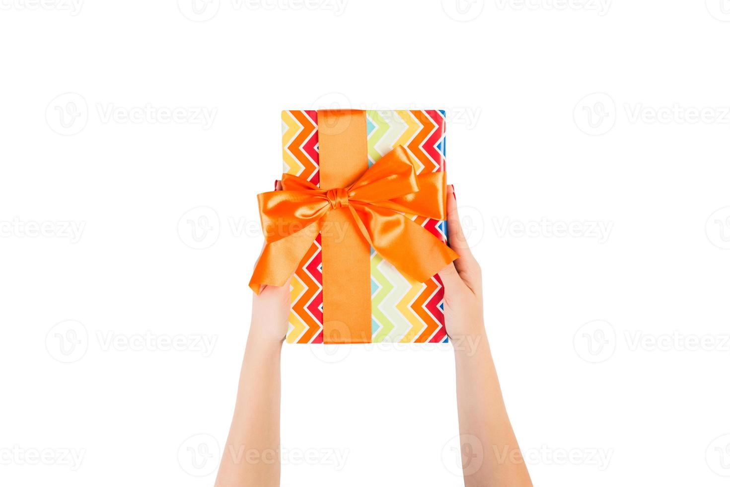 Woman hands give wrapped Christmas or other holiday handmade present in colored paper with orange ribbon. Isolated on white background, top view. thanksgiving Gift box concept photo