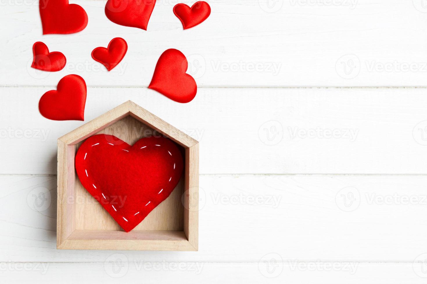 composición de vista superior hecha de corazón rojo en una casa rodeada de pequeños corazones sobre fondo de madera. concepto de hogar dulce hogar. día de San Valentín foto
