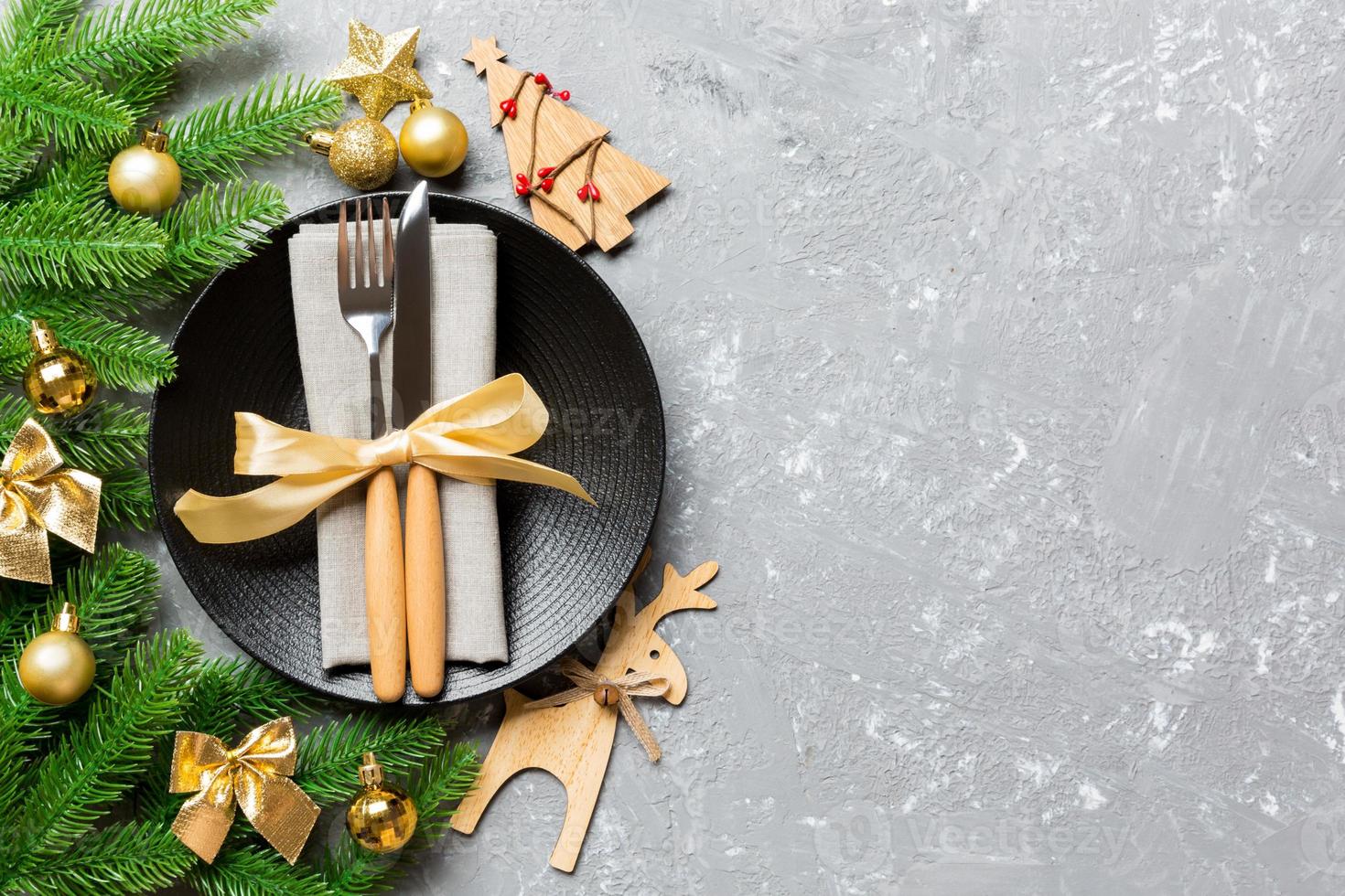 Top view of New Year dinner on festive cement background. Composition of plate, fork, knife, fir tree and decorations. Merry Christmas concept photo