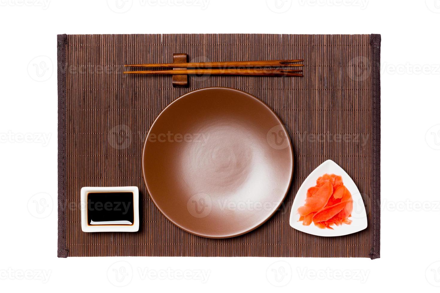 Empty round brown plate with chopsticks for sushi, ginger and soy sauce on dark bamboo mat background. Top view with copy space for you design photo