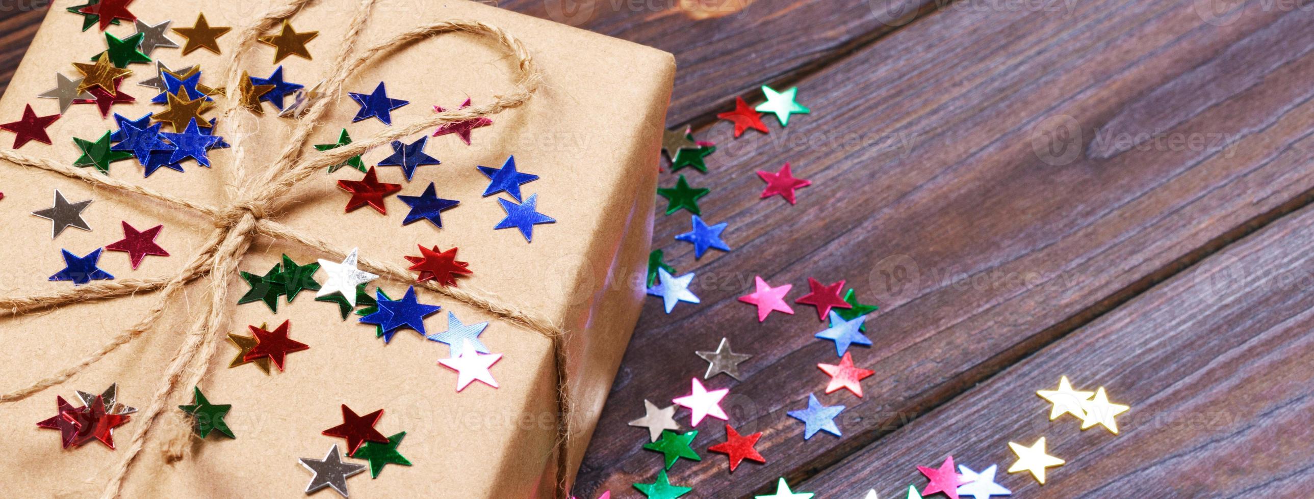 Gift box with star. Creative concept with festive decor on black background. Confetti stars, red, yellow with gift box. Explosion of confetti photo