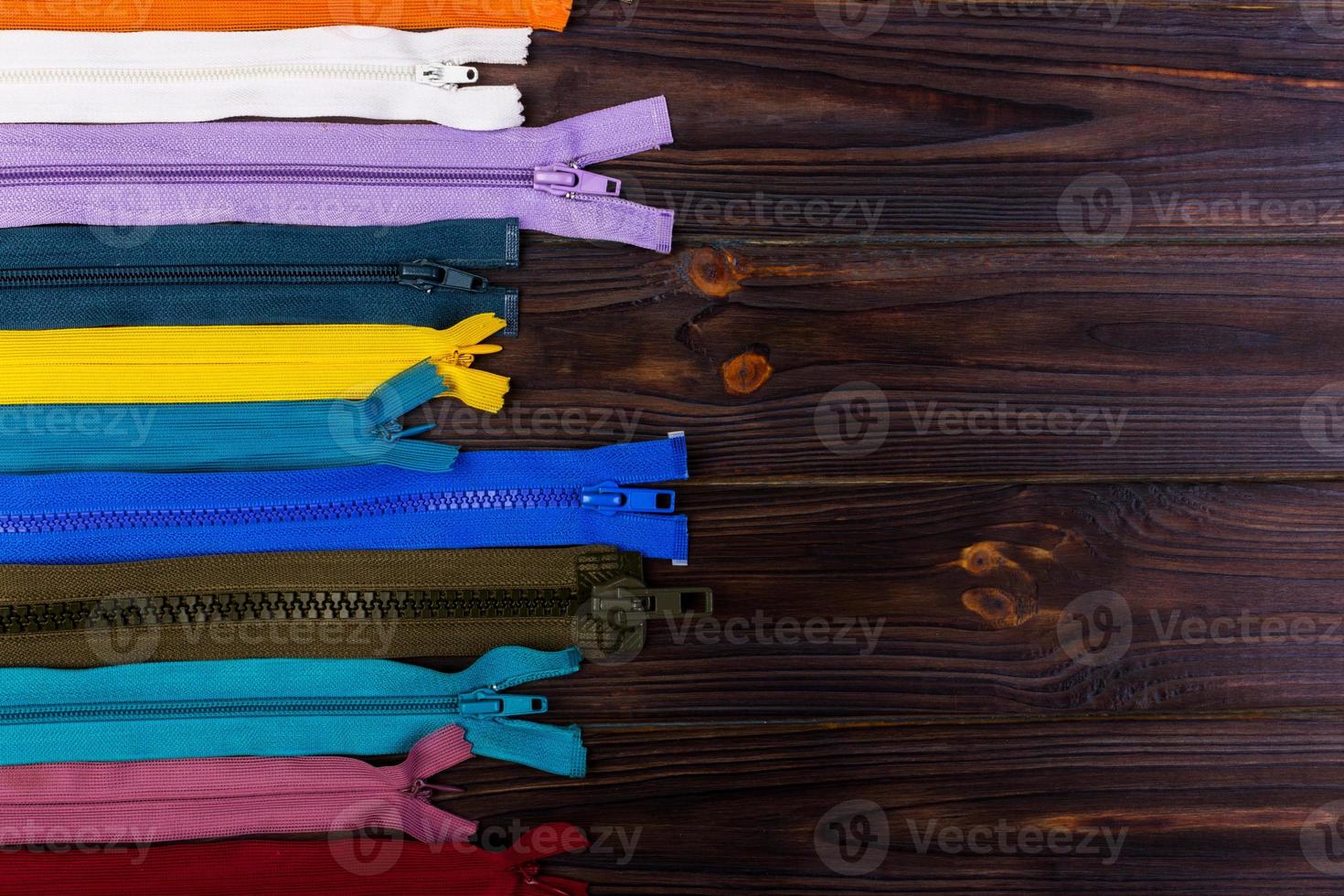 Multicolored zippers are laid out on a wooden table photo