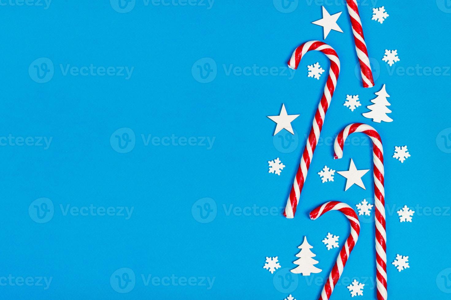 Christmas candy cane lied evenly in row on blue background with decorative snowflake and star. Flat lay and top view photo