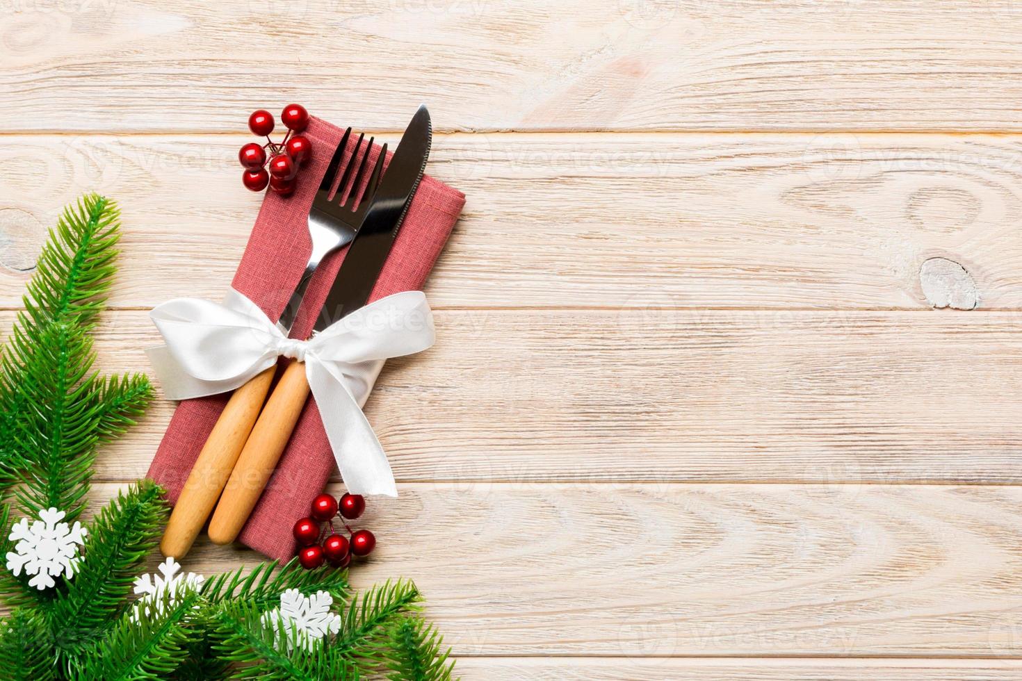 Top view of christmas decorations on wooden background. Fork and knife on napkin tied up with ribbon and empty space for your design. New year pattern concept photo