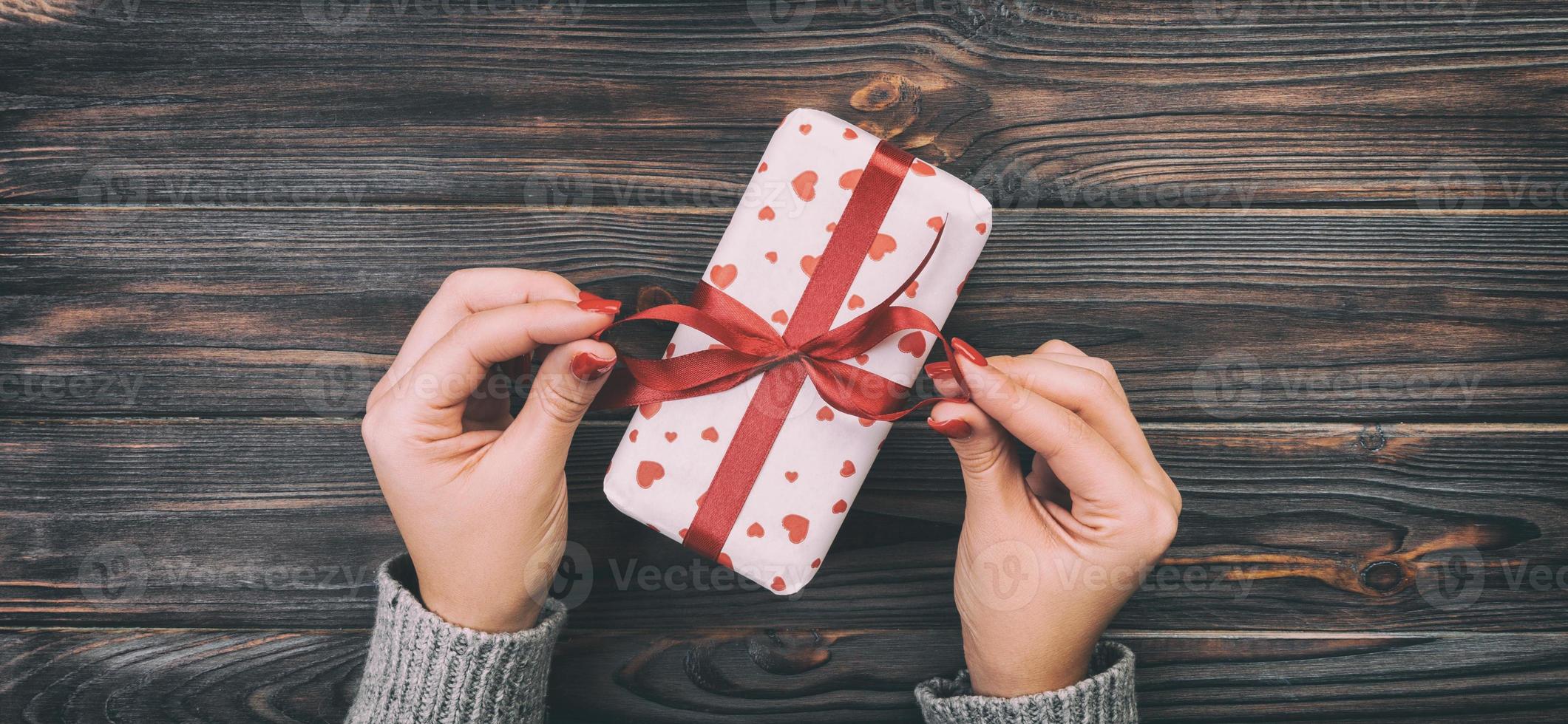 Woman hands giving Holidays gift box on wood table, Present box, red heart decoration of gift on wooden table, top view with copy space for you design. Toned web banner photo