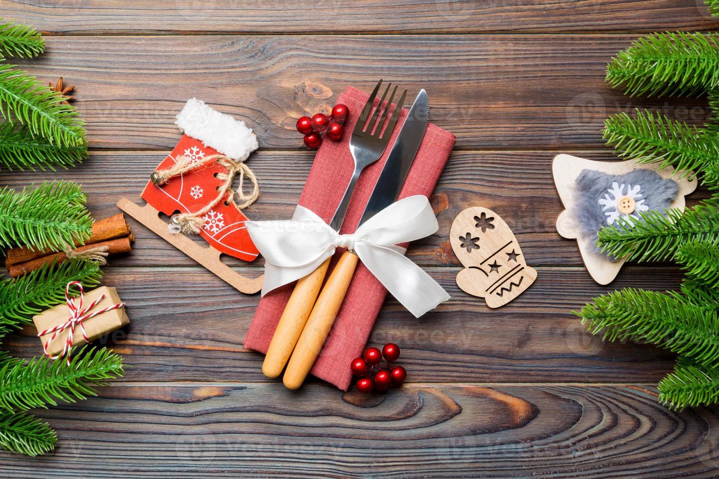 Top view of christmas decorations on wooden background. Close up of fork and knife on napkin tied up with ribbon. New year pattern concept photo