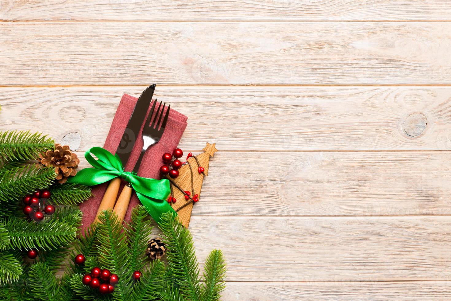 Top view of fork and knife on napkin with christmas decorations and new year tree on wooden background. Holiday and festive concept with copy space photo