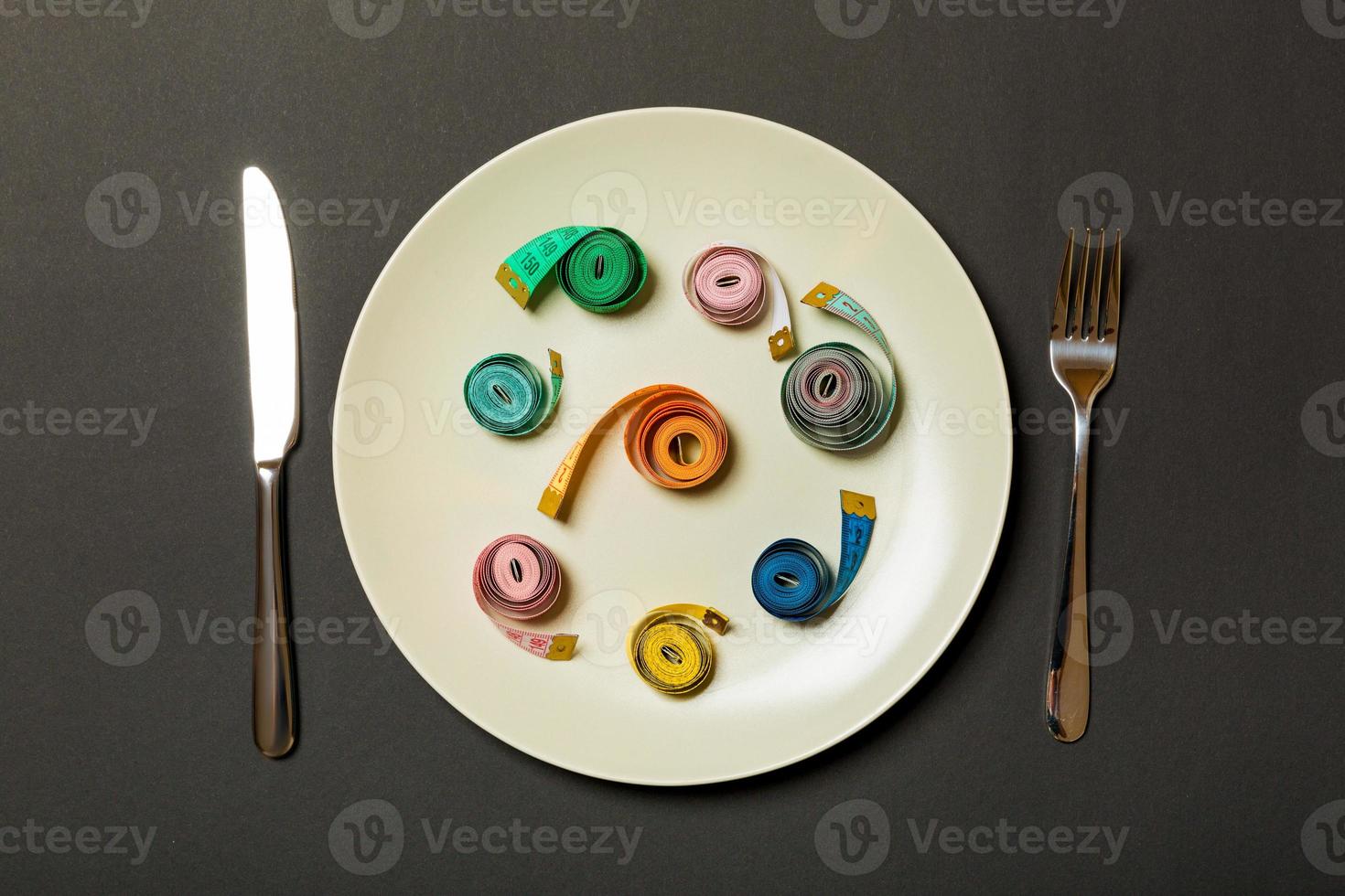 Measuring tape in a plate with fork and knife on both sides on black background. Top view of weight loss concept photo