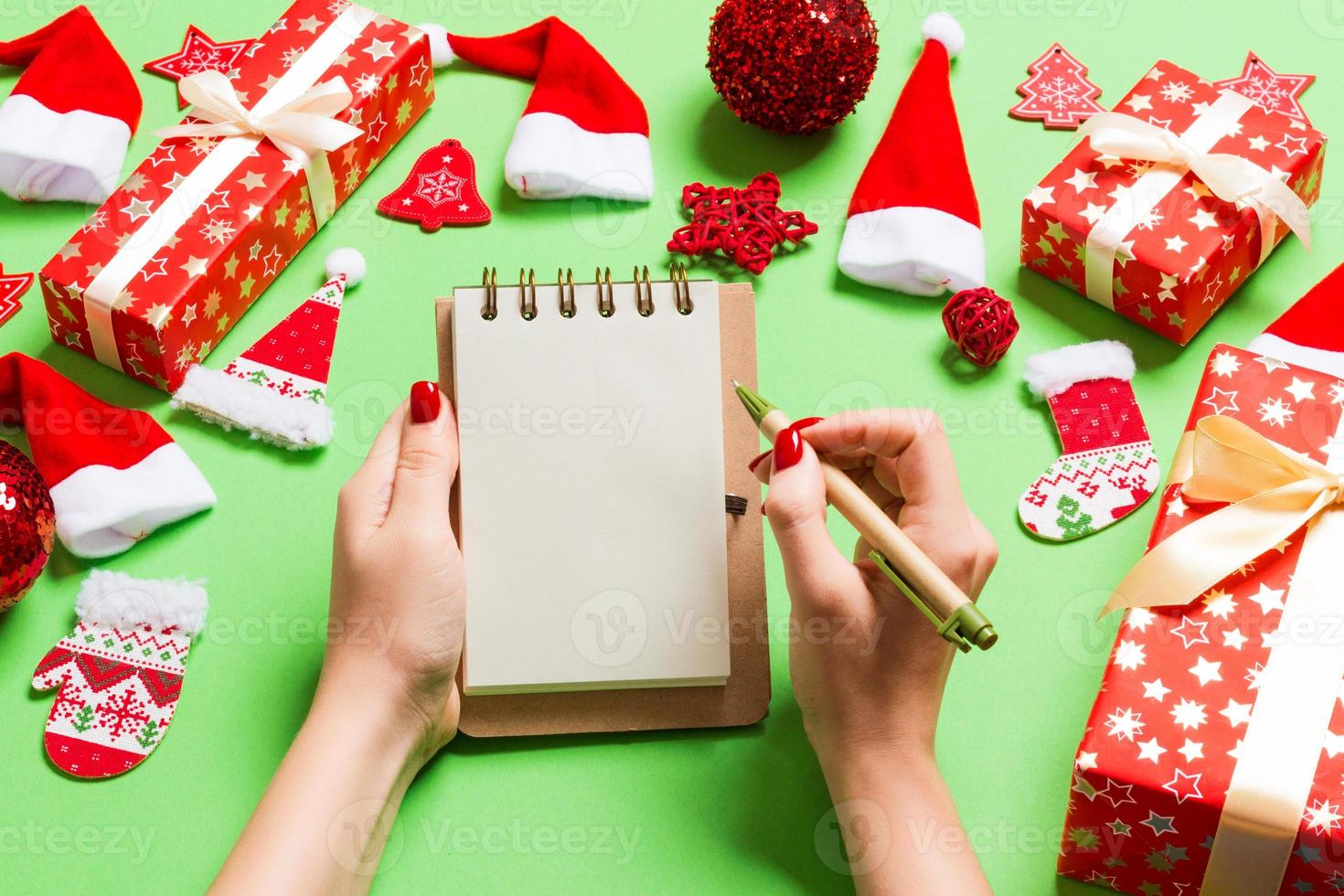 Top view of female hand making some notes in noteebok on green background. New Year decorations and toys. Christmas time concept photo
