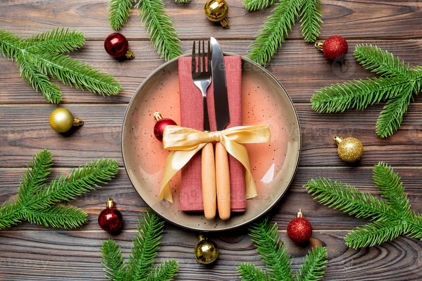 Top view of New Year dinner on festive wooden background. Composition of plate, fork, knife, fir tree and decorations. Merry Christmas concept photo
