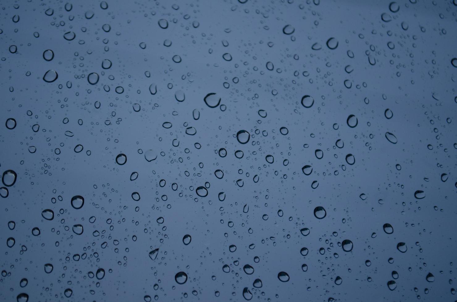 gotas de lluvia azul en la ventana. concepto triste y de mal humor con colores sombríos. gotas de agua sobre fondo transparente en días lluviosos en la noche. tiempo tormentoso. aislamiento triste depresión concepto. foto