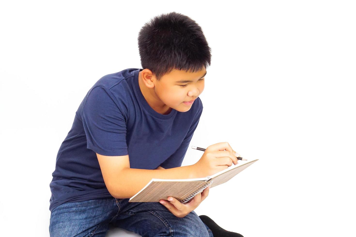 Young boy sitting on white background and writing a book. Education and learning concept. photo