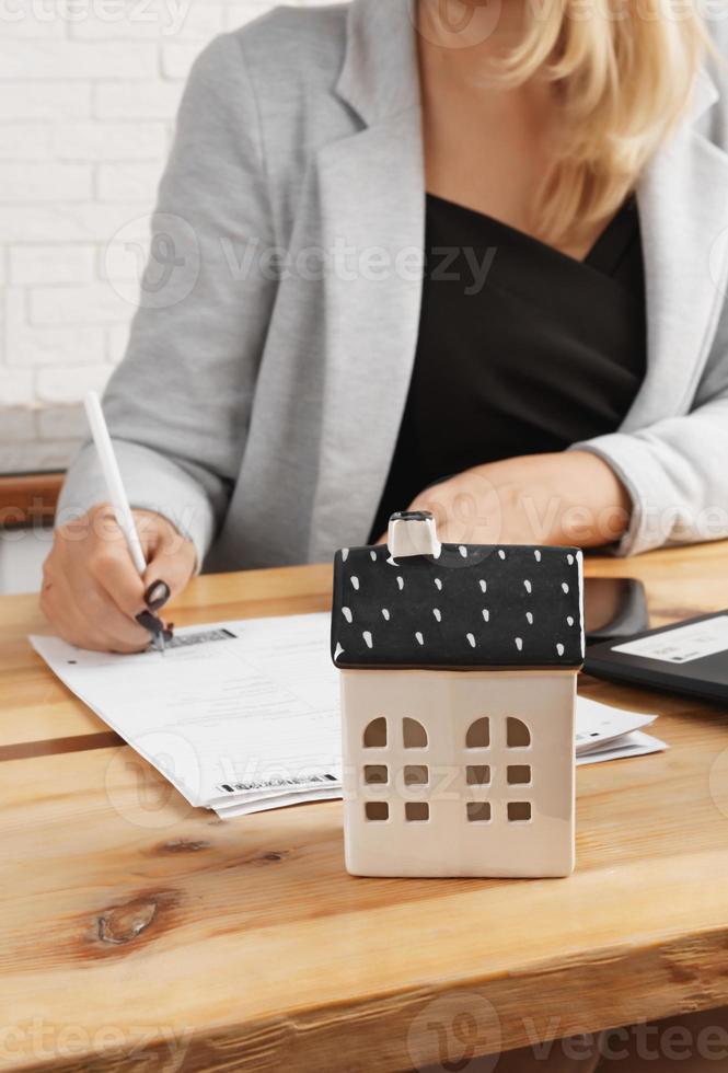 A business lady signs documents against the background of a house model against the background of kitchen furniture. photo