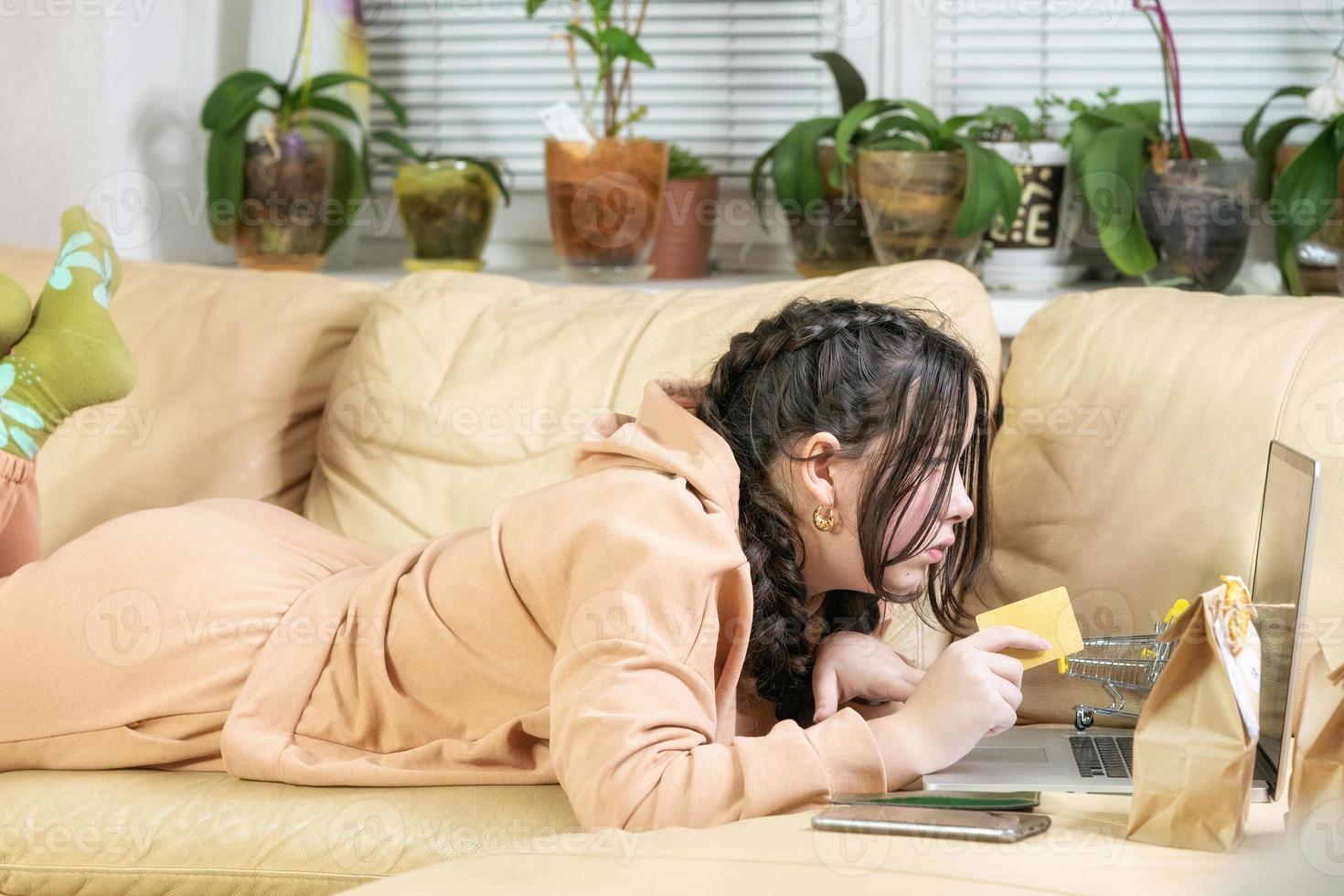 Smiling girl at home, she is relaxing on the couch and shopping online using a credit card photo