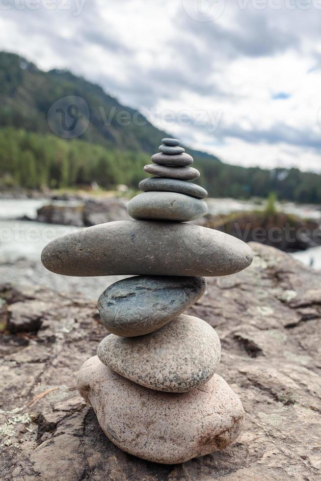 A pyramid of bare stones stacked on top of each other. Stones stacked in the shape of a pyramid on the riverbank against the background of mountains as balance and balance in nature, Zen, Buddhism. photo
