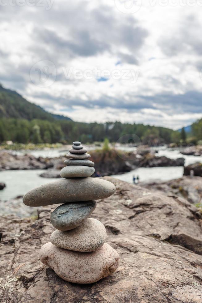 A pyramid of bare stones stacked on top of each other. Stones stacked in the shape of a pyramid on the riverbank against the background of mountains as balance and balance in nature, Zen, Buddhism. photo