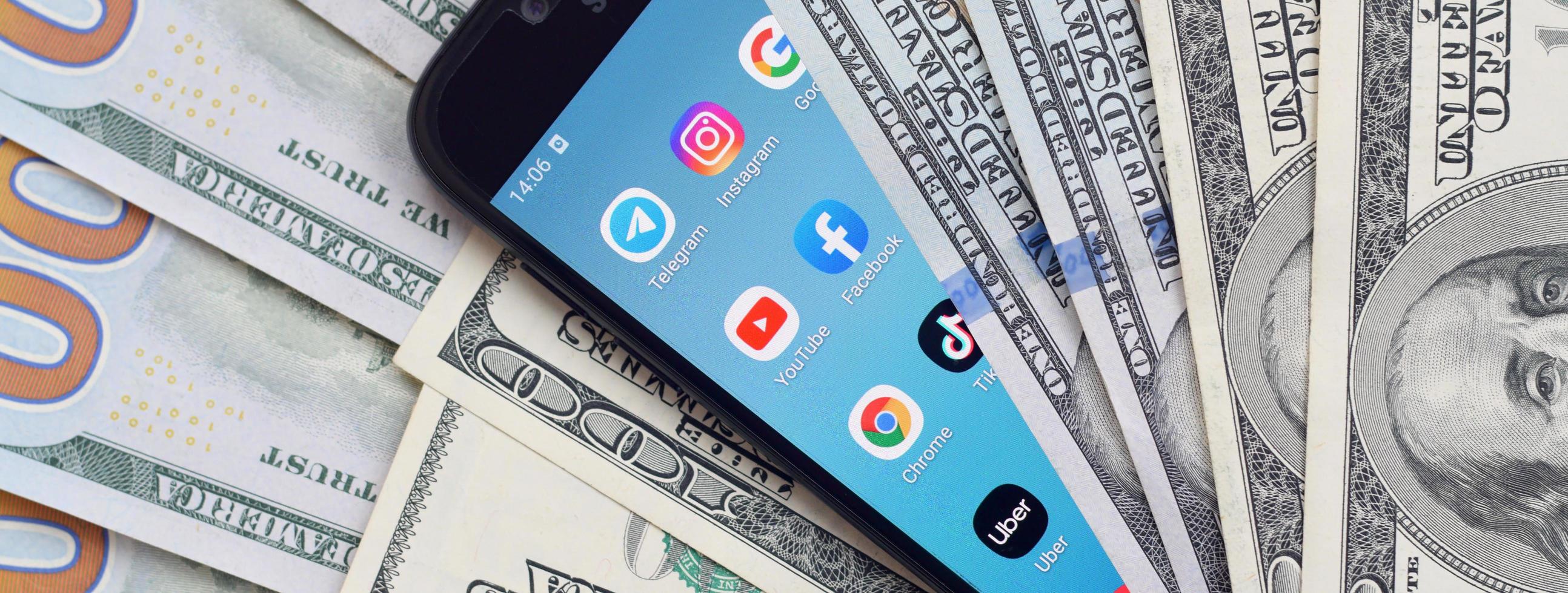 KHARKOV, UKRAINE - MAY 12, 2022 Smartphone screen with many popular apps and lot of hundred dollar bills. Business and social networking concept photo