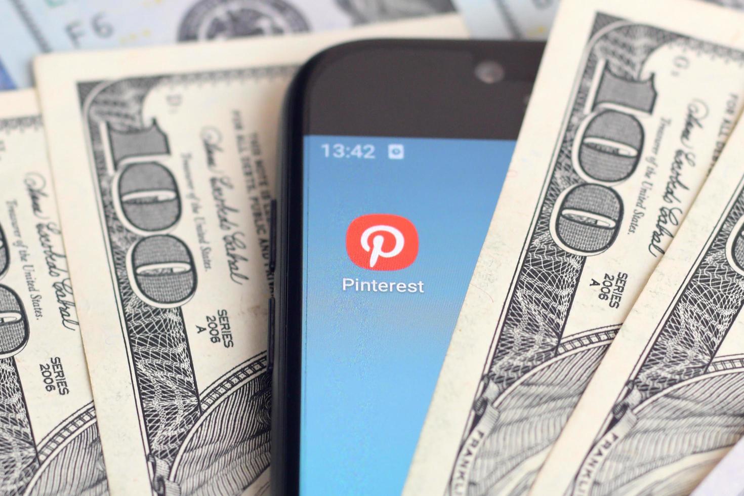 KHARKOV, UKRAINE - MAY 12, 2022 Smartphone screen with Pinterest app and lot of hundred dollar bills. Business and social networking concept photo