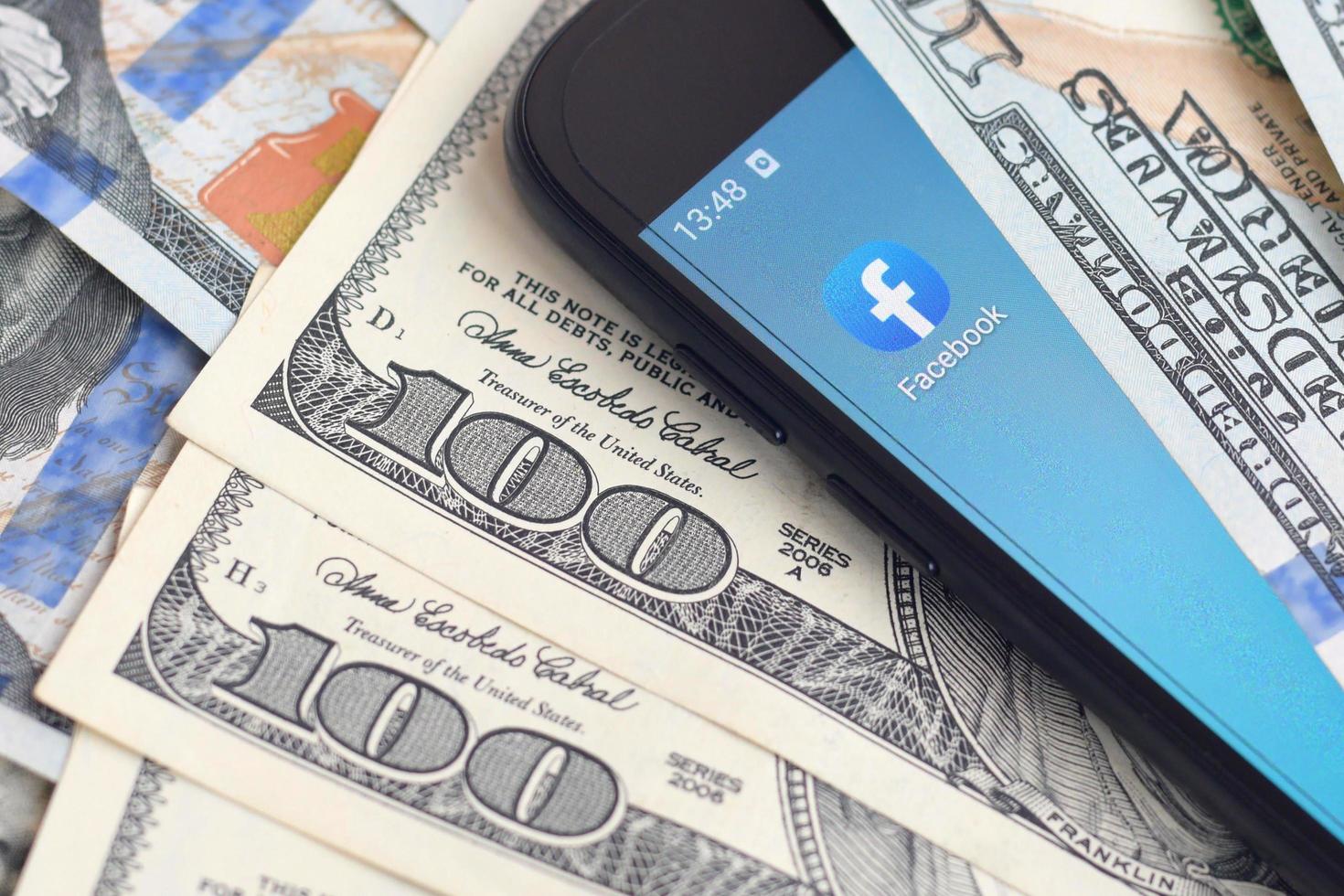 KHARKOV. UKRAINE - MAY 17, 2022 Smartphone screen with Facebook app and lot of hundred dollar bills. Business and social networking concept photo