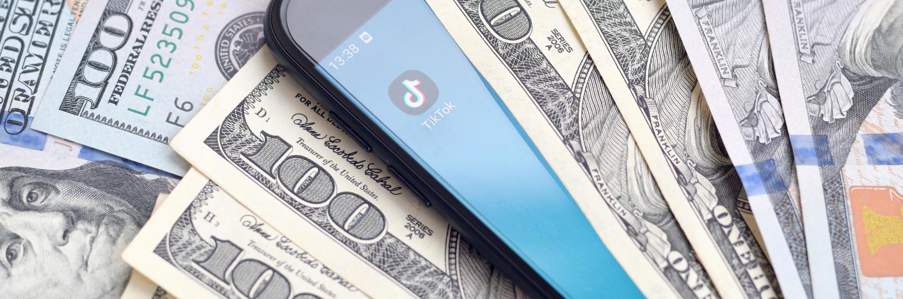 KHARKOV. UKRAINE - MAY 17, 2022 Smartphone screen with Tiktok app and lot of hundred dollar bills. Business and social networking concept photo