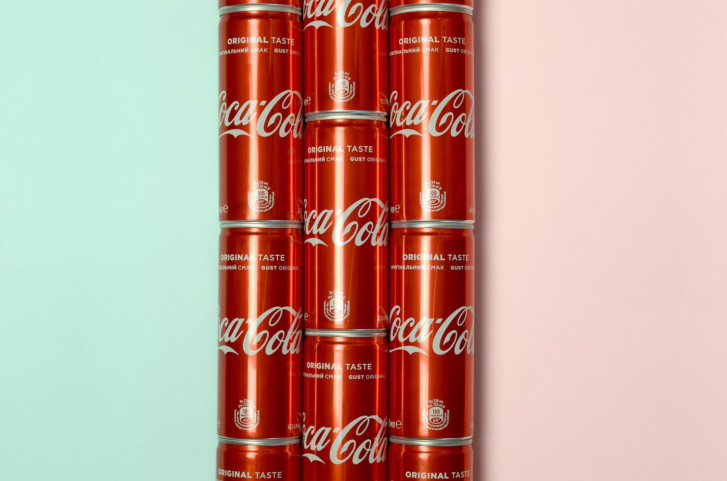 KHARKOV. UKRAINE - MAY 2, 2022 Flat lay shot carbonated red drink tin cans Coca Cola laying on pastel blue and coral background photo