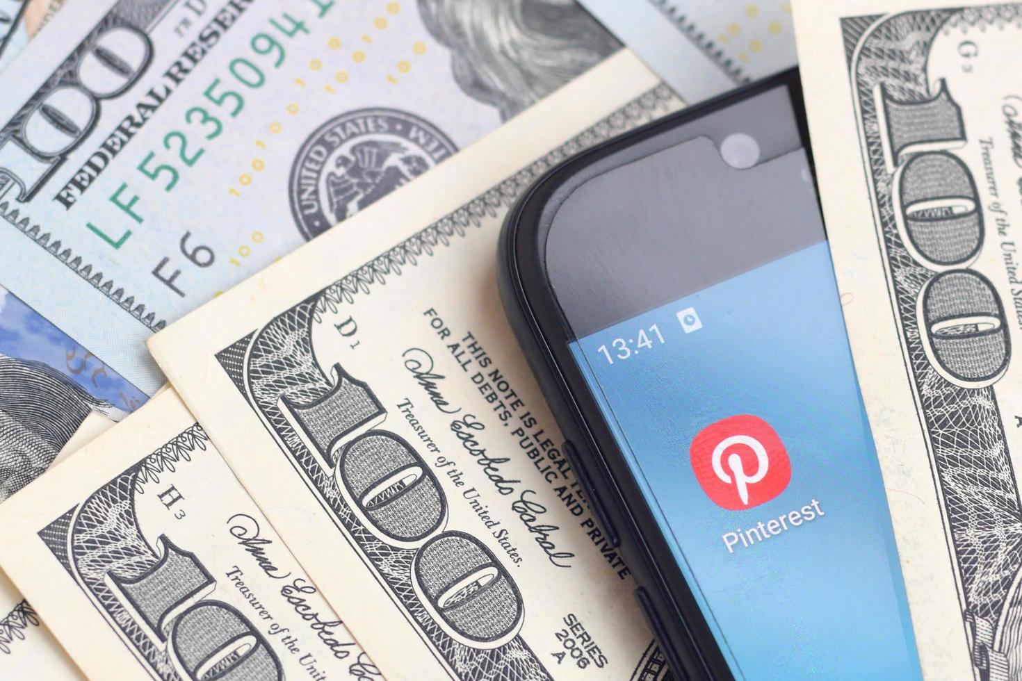 KHARKOV, UKRAINE - MAY 3, 2022 Smartphone screen with Pinterest app and lot of hundred dollar bills. Business and social networking concept photo
