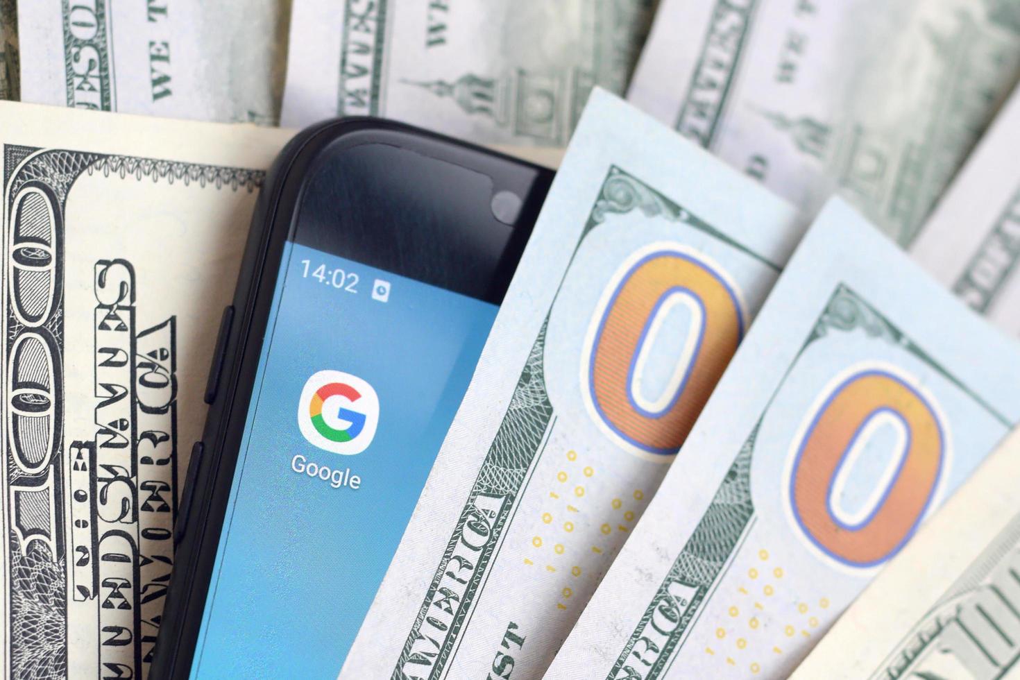 KHARKOV, UKRAINE - MAY 3, 2022 Smartphone screen with Google app and lot of hundred dollar bills. Business and social networking concept photo