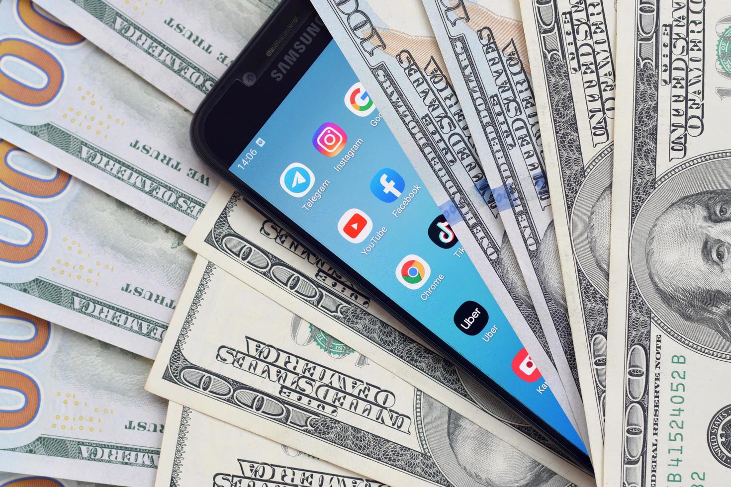 KHARKOV, UKRAINE - MAY 12, 2022 Smartphone screen with many popular apps and lot of hundred dollar bills. Business and social networking concept photo