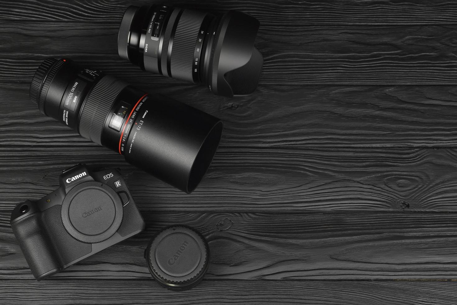 KHARKOV, UKRAINE - DECEMBER 27, 2022 Canon EOS R photocamera and mount adapter EF - EOS R with Canon 105mm f2.8 and Sigma 24-105 f4 Art lenses on black wooden table photo