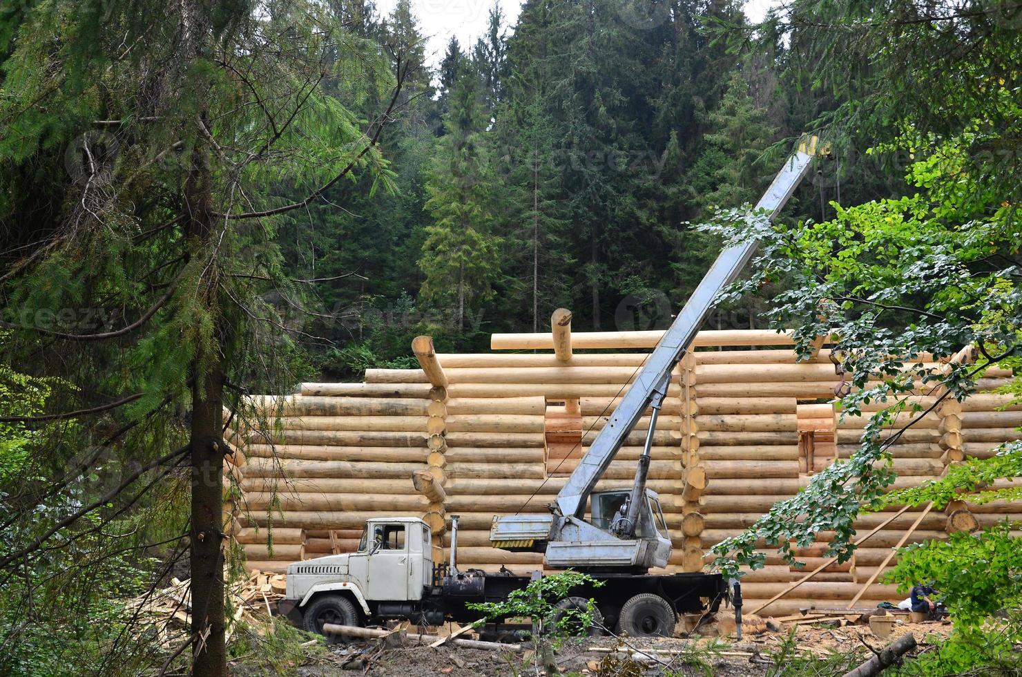 el proceso de construcción de una casa de madera a partir de vigas de madera de forma cilíndrica. grúa en condiciones de trabajo foto