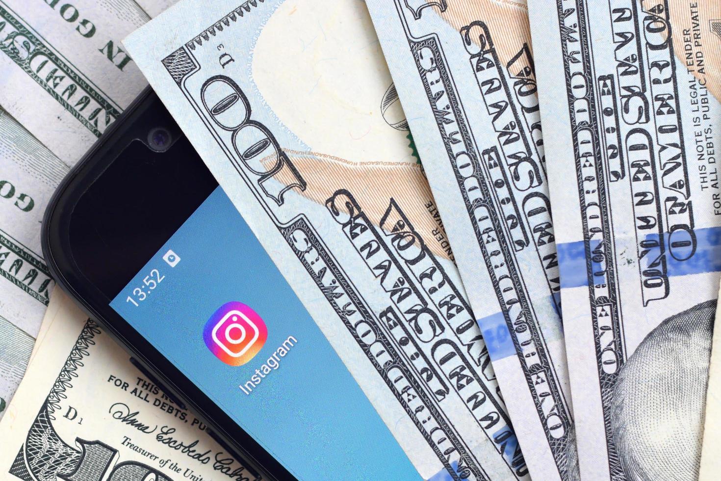KHARKOV, UKRAINE - MAY 12, 2022 Smartphone screen with Instagram app and lot of hundred dollar bills. Business and social networking concept photo