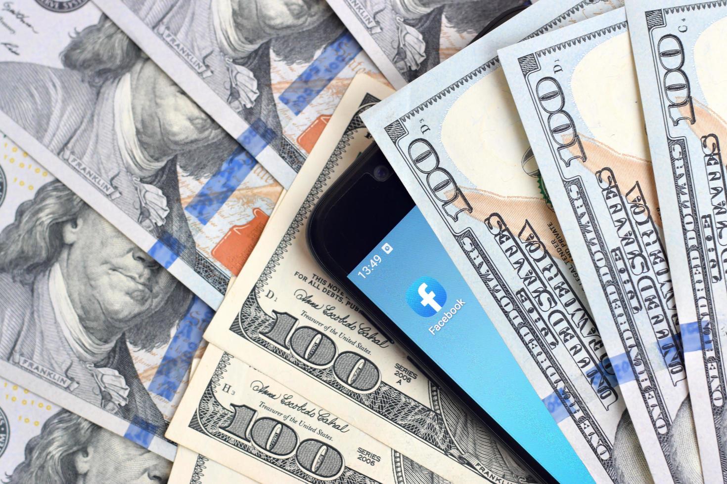 KHARKOV, UKRAINE - MAY 12, 2022 Smartphone screen with Facebook app and lot of hundred dollar bills. Business and social networking concept photo