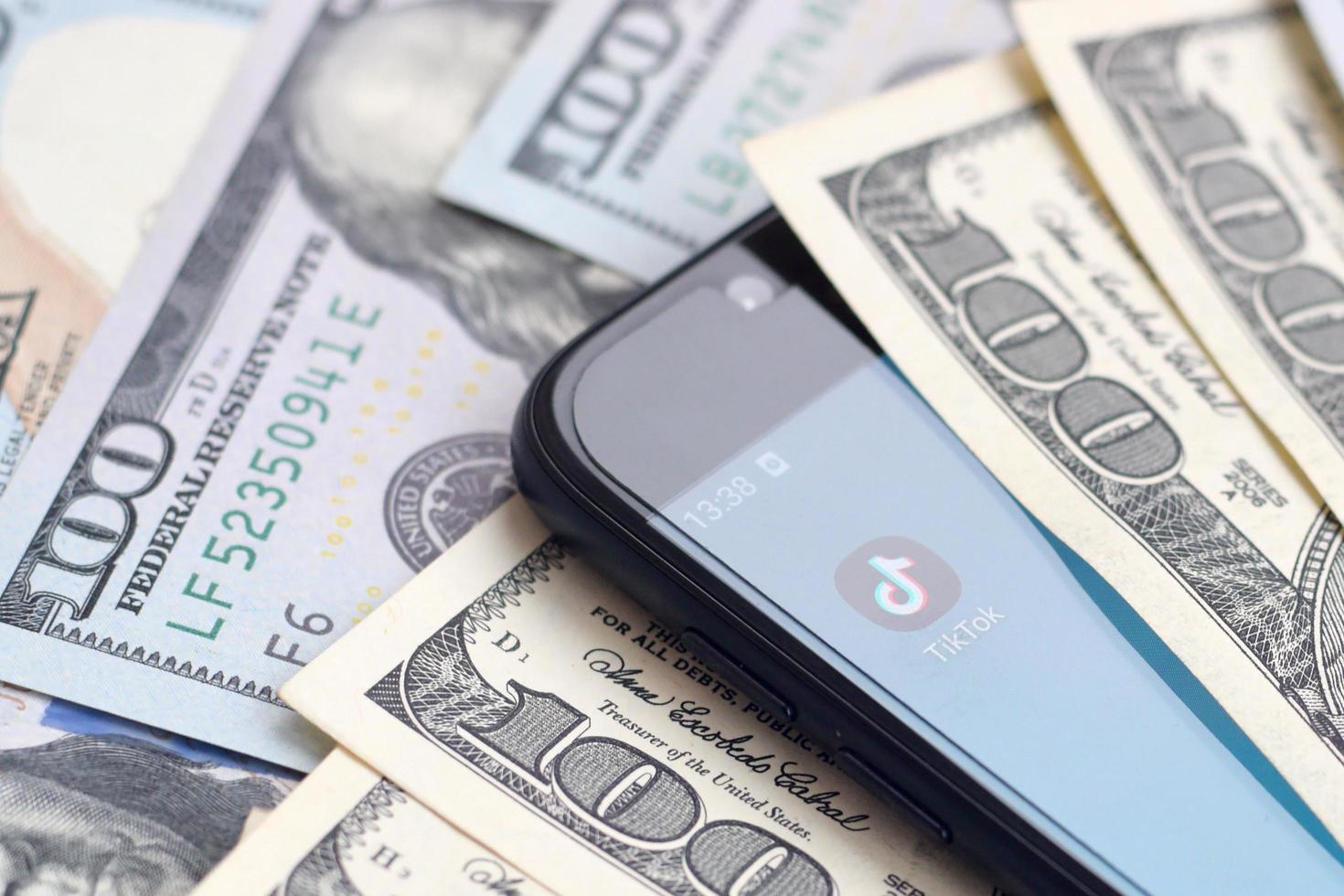 KHARKOV, UKRAINE - MAY 12, 2022 Smartphone screen with Tiktok app and lot of hundred dollar bills. Business and social networking concept photo