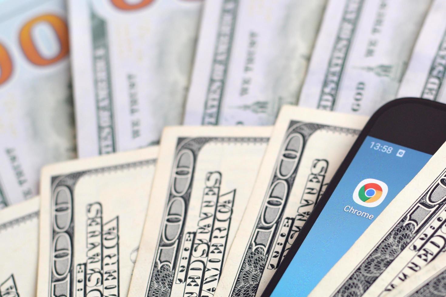 KHARKOV, UKRAINE - MAY 12, 2022 Smartphone screen with Google chrome app and lot of hundred dollar bills. Business and social networking concept photo