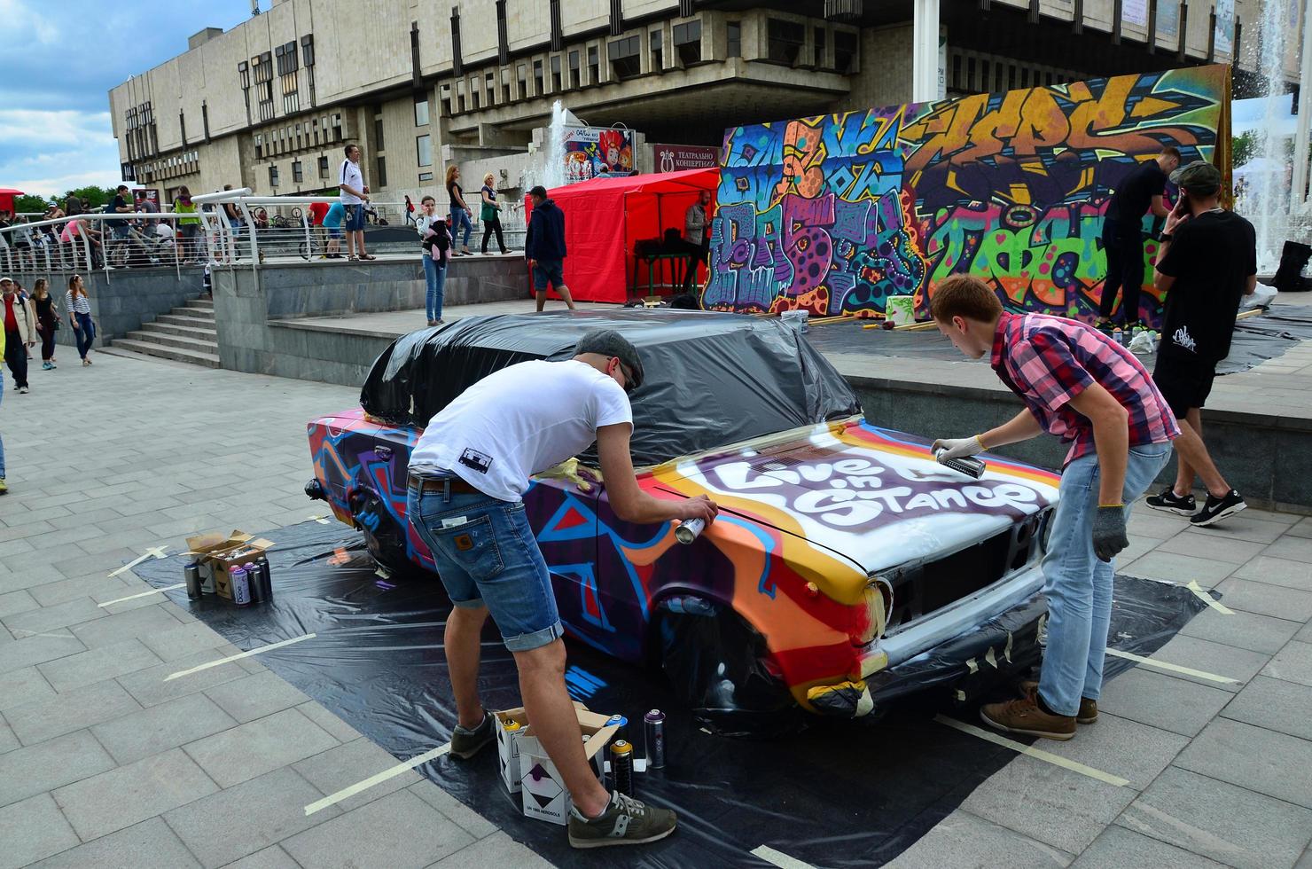 KHARKOV, UKRAINE - MAY 27, 2022 Festival of street art. Young guys draw graffiti on the car body in the city center. The process of drawing color graffiti on a car with aerosol cans photo