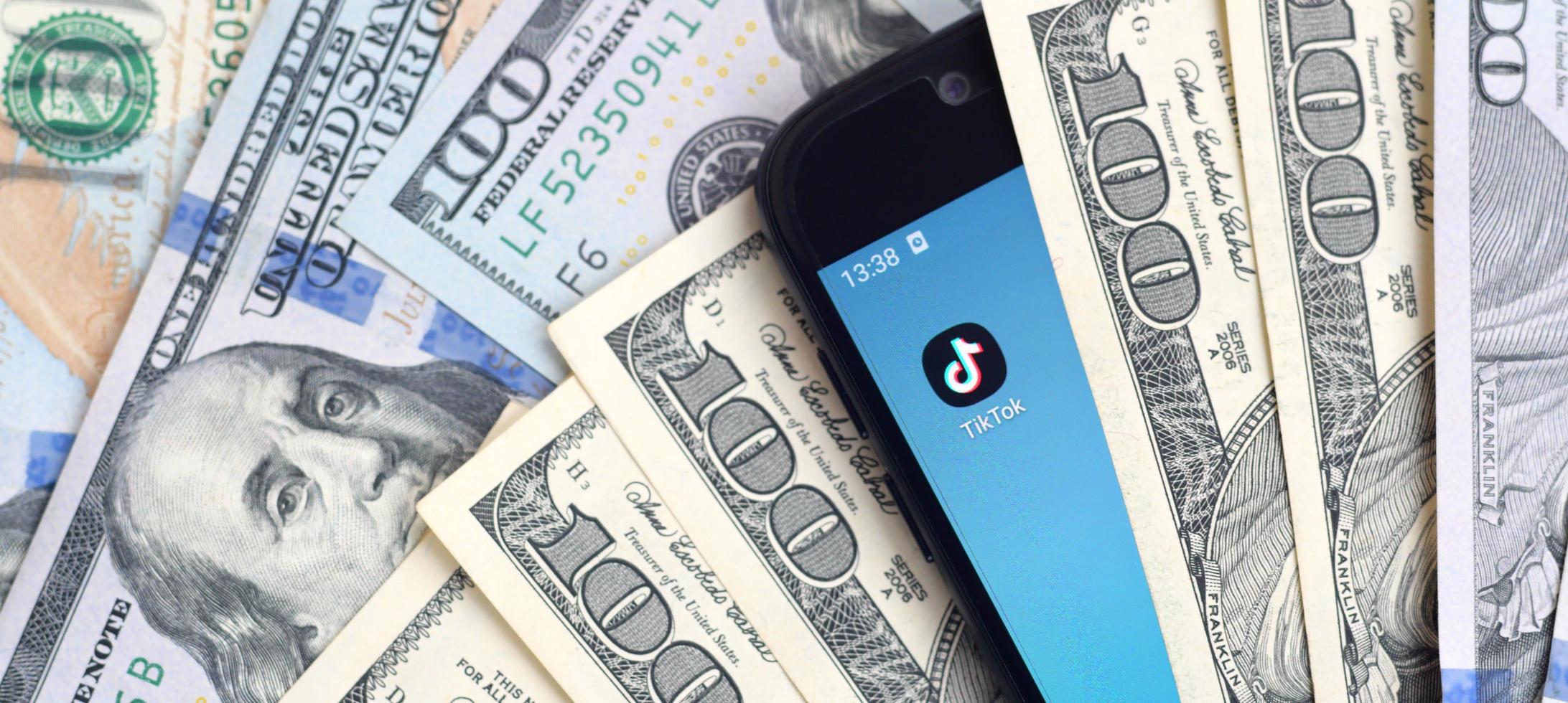 KHARKOV, UKRAINE - MAY 3, 2022 Smartphone screen with Tiktok app and lot of hundred dollar bills. Business and social networking concept photo