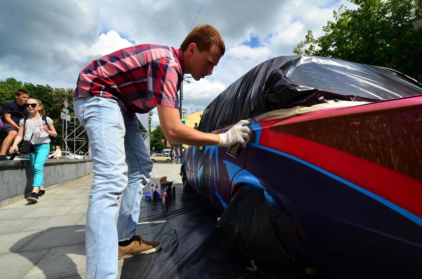 KHARKOV. UKRAINE - MAY 2, 2022 Festival of street art. Young guys draw graffiti on the car body in the city center. The process of drawing color graffiti on a car with aerosol cans photo