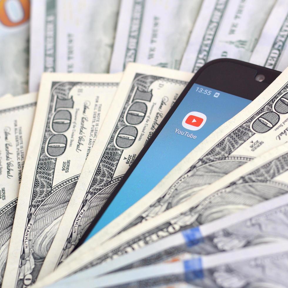 KHARKOV, UKRAINE - MAY 12, 2022 Smartphone screen with Youtube app and lot of hundred dollar bills. Business and social networking concept photo