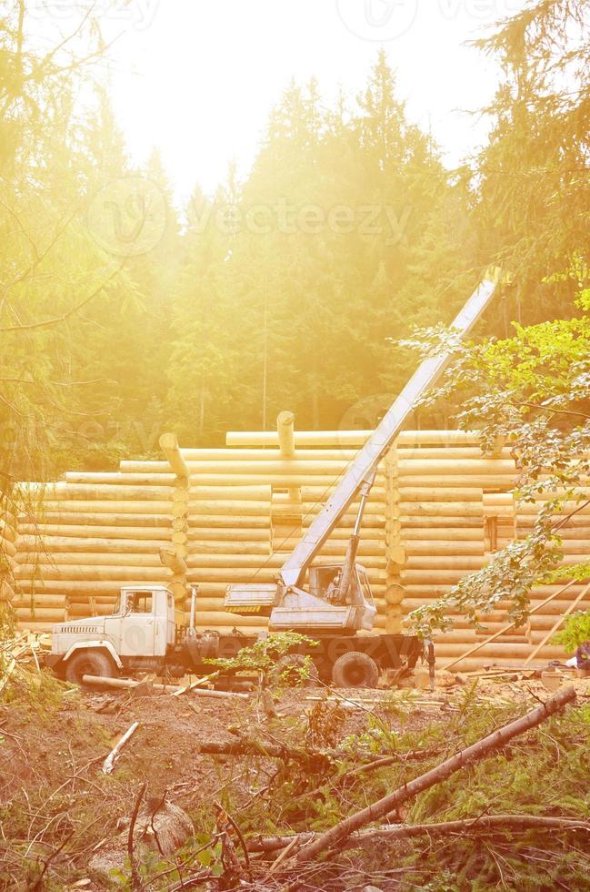 el proceso de construcción de una casa de madera a partir de vigas de madera de forma cilíndrica. grúa en condiciones de trabajo foto