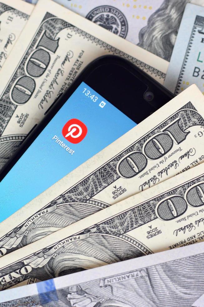 KHARKOV, UKRAINE - MAY 12, 2022 Smartphone screen with Pinterest app and lot of hundred dollar bills. Business and social networking concept photo