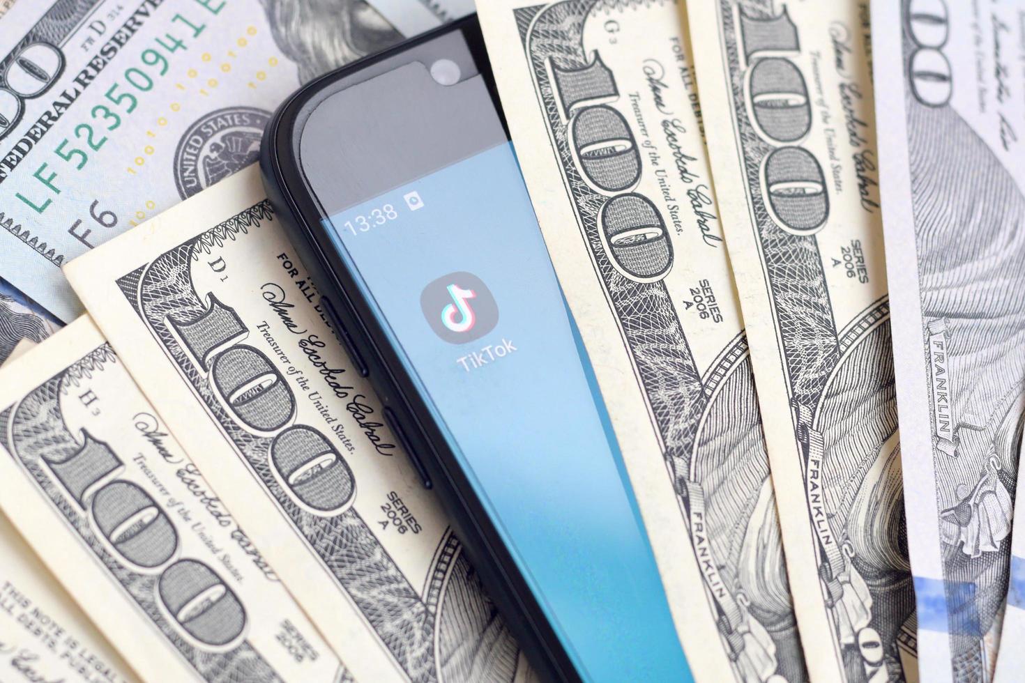 KHARKOV, UKRAINE - MAY 3, 2022 Smartphone screen with Tiktok app and lot of hundred dollar bills. Business and social networking concept photo