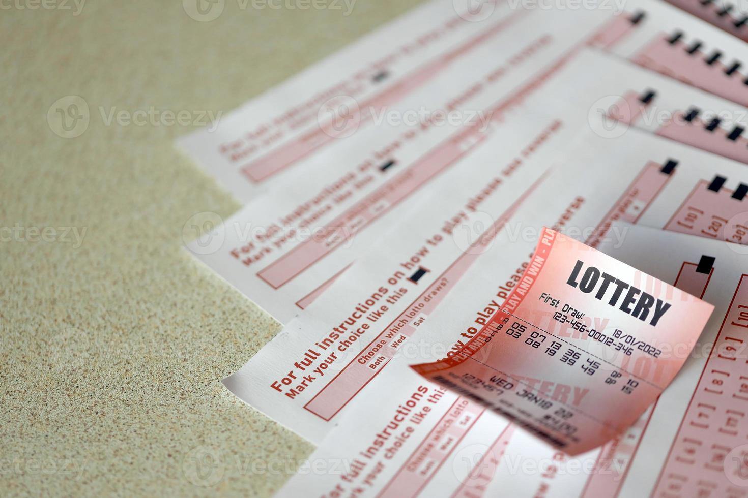 Red lottery ticket lies on pink gambling sheets with numbers for marking to play lottery. Lottery playing concept or gambling addiction. Close up photo