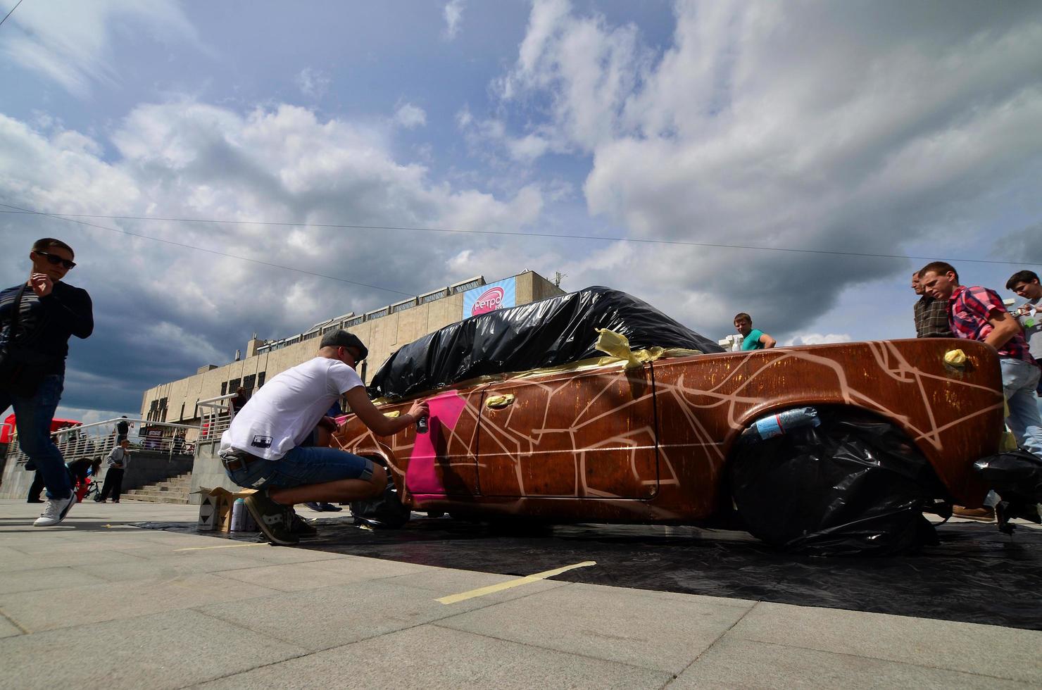 KHARKOV, UKRAINE - MAY 27, 2022 Festival of street art. Young guys draw graffiti on the car body in the city center. The process of drawing color graffiti on a car with aerosol cans photo