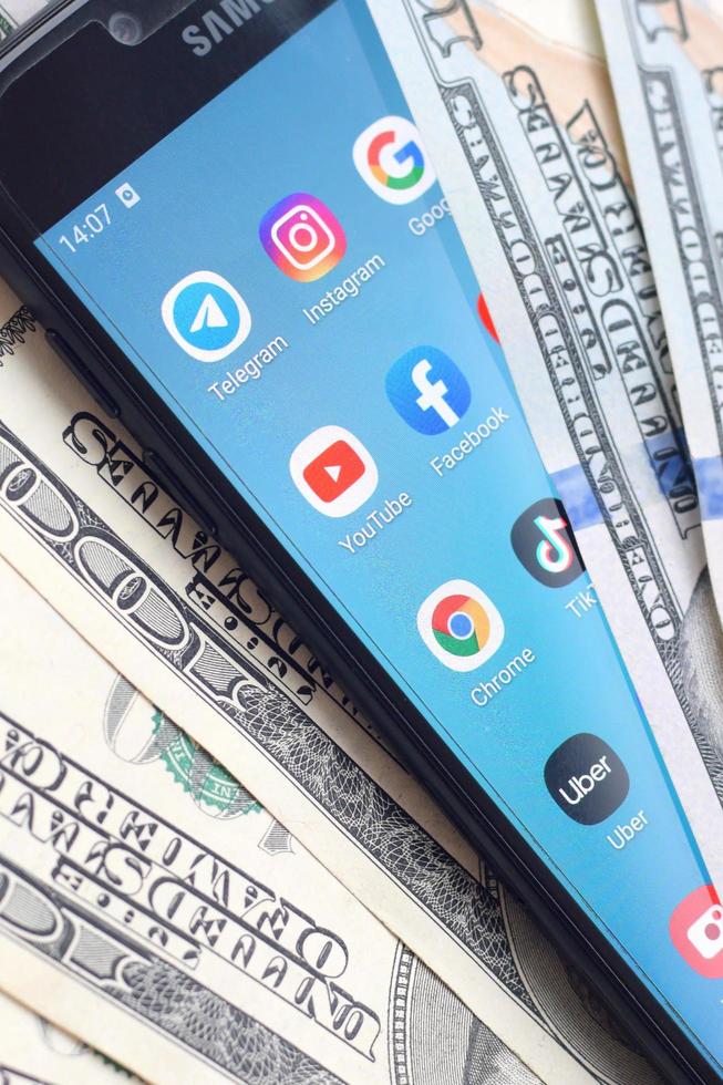 KHARKOV, UKRAINE - MAY 3, 2022 Smartphone screen with many popular apps and lot of hundred dollar bills. Business and social networking concept photo