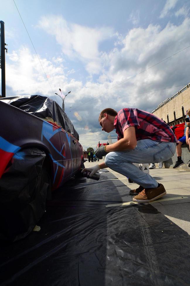 KHARKOV, UKRAINE - MAY 27, 2022 Festival of street art. Young guys draw graffiti on the car body in the city center. The process of drawing color graffiti on a car with aerosol cans photo