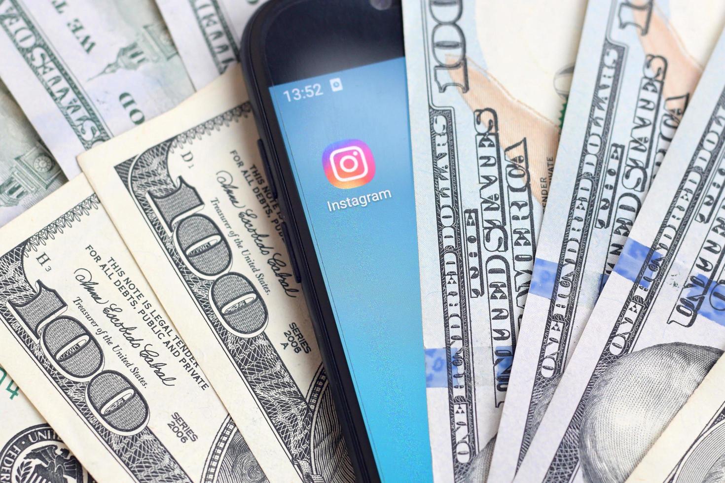 KHARKOV, UKRAINE - MAY 3, 2022 Smartphone screen with Instagram app and lot of hundred dollar bills. Business and social networking concept photo