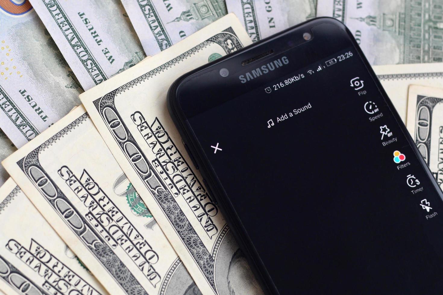 KHARKOV, UKRAINE - MAY 12, 2022 Smartphone screen with Tiktok app and lot of hundred dollar bills. Business and social networking concept photo