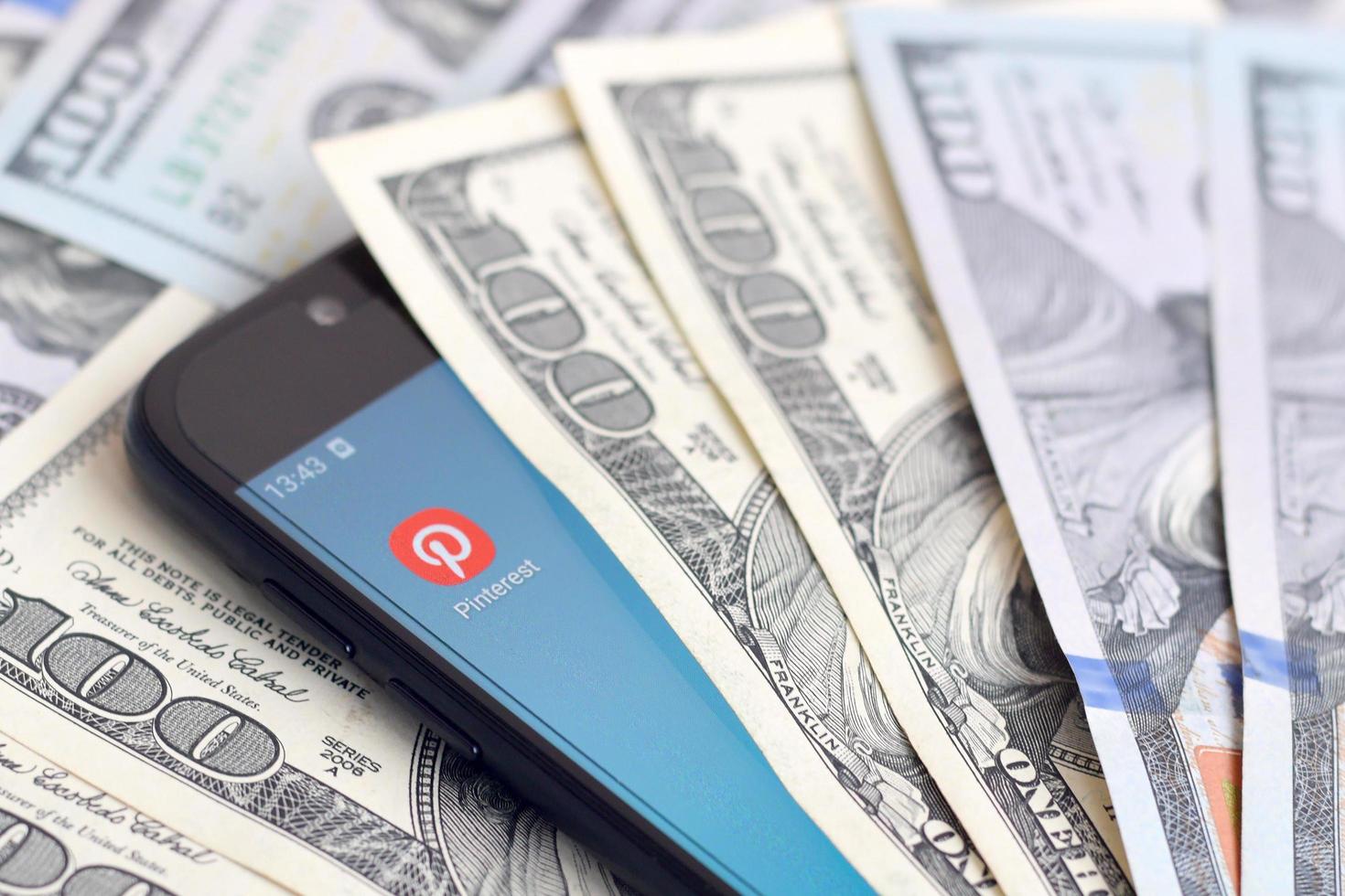 KHARKOV. UKRAINE - MAY 17, 2022 Smartphone screen with Pinterest app and lot of hundred dollar bills. Business and social networking concept photo