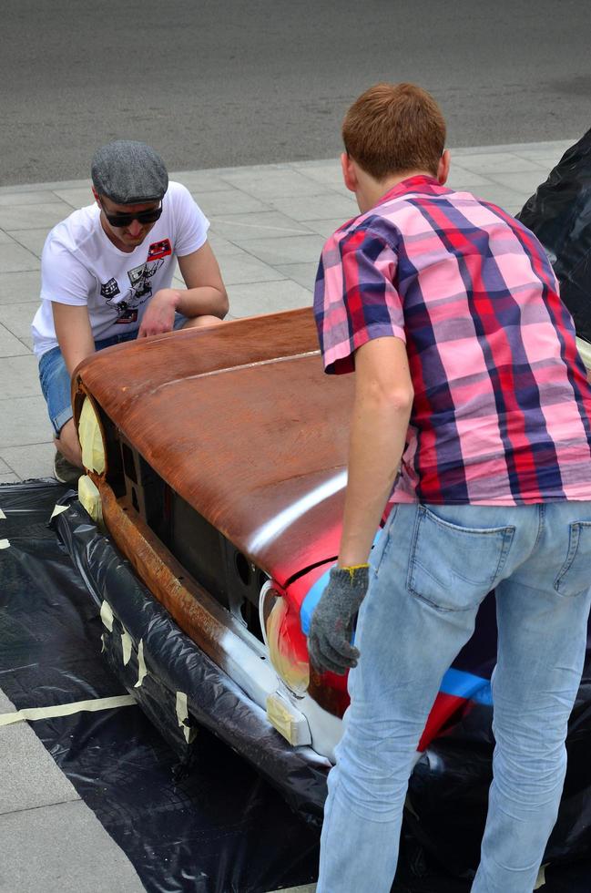 KHARKOV, UKRAINE - MAY 27, 2022 Festival of street art. Young guys draw graffiti on the car body in the city center. The process of drawing color graffiti on a car with aerosol cans photo